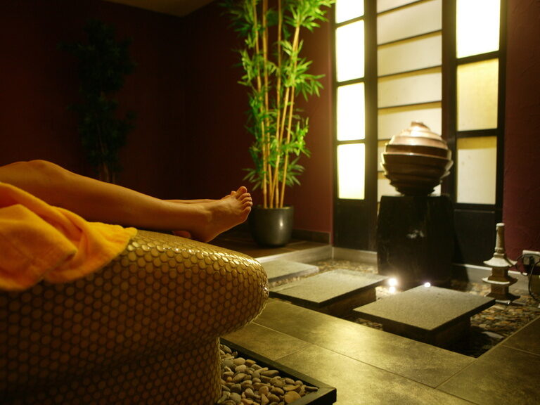 Entspannte Person auf beheizter Steinliege mit warmer Decke im Spa des Hotel Der Heidehof