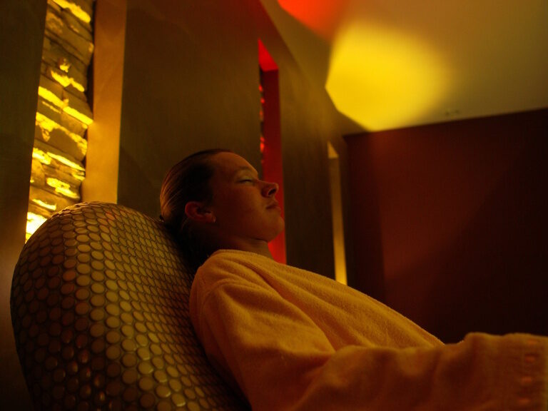Wellnessgast in orangefarbenem Bademantel im stimmungsvoll beleuchteten Ruheraum mit Salzsteinwand im Heidehof Spa